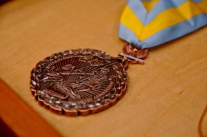 Image showing the Order of St. Maurice Award, which is a bronze medal with a blue and yellow ribbon attached.